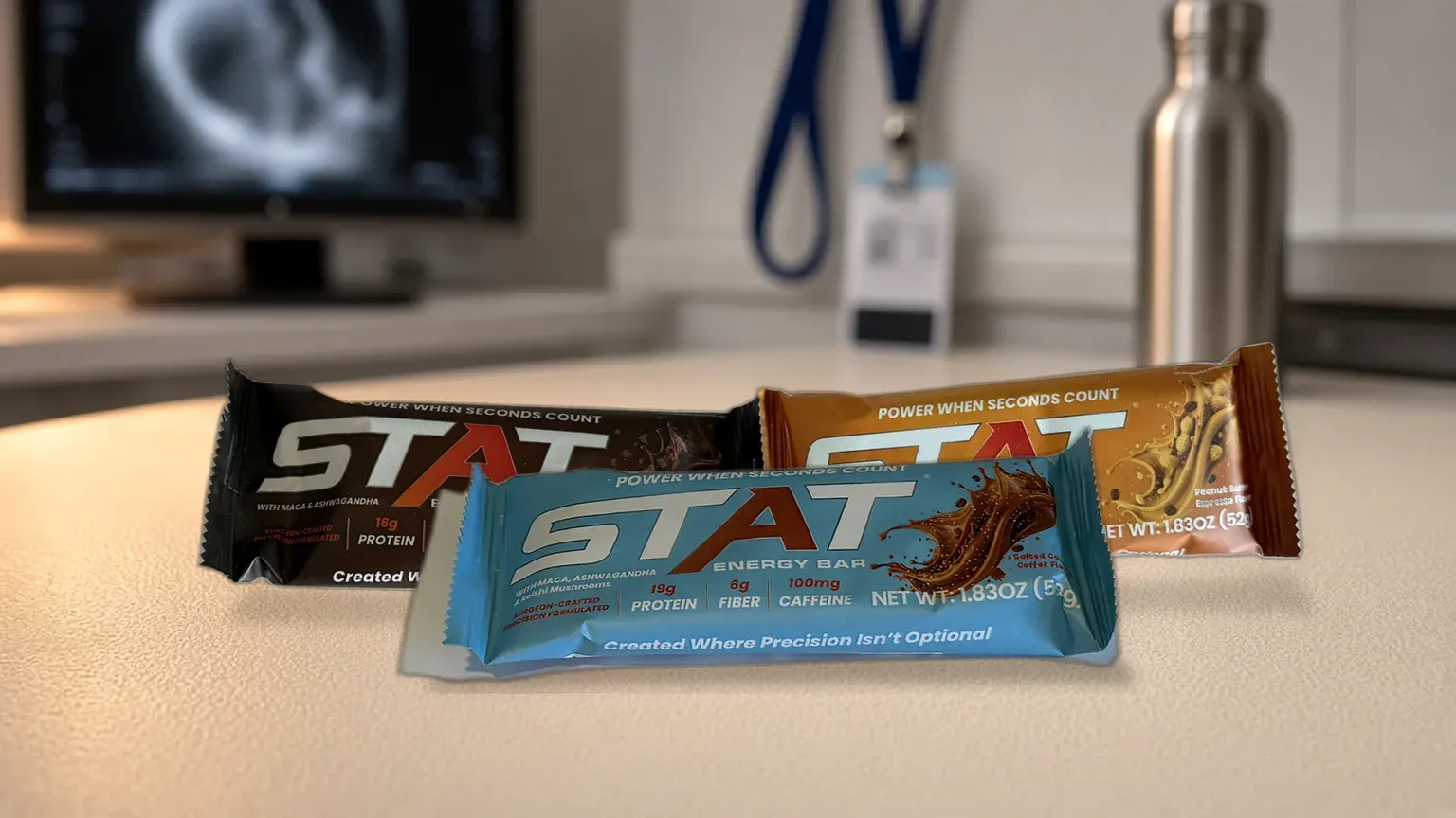 STAT Salted Caramel Coffee Energy Bar on a cream radiology desk between studies, with Chocolate and Peanut Butter Espresso bars behind; warm copper light, imaging monitor softly blurred in the background.